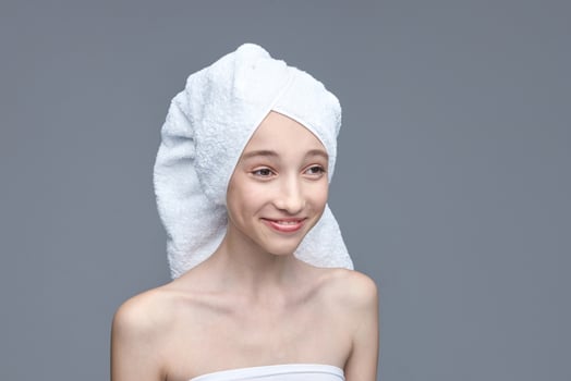Young caucasian female with towel wrapped hair smiling on gray background. photo