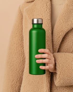 Green Stainless Steel Water Bottle Held by a Woman in a Beige Coat. A Stylish and Sustainable Hydration Solution for Everyday Use photo