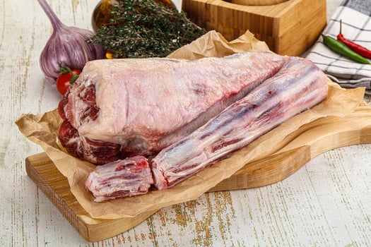 A raw lamb leg on a cutting board with vegetables photo