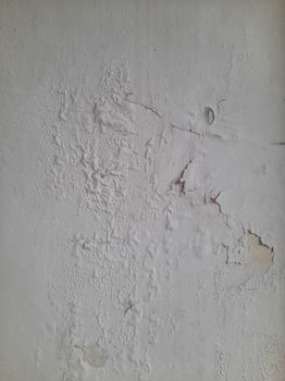Old peeling wall texture with cracked, blistered, and flaking white paint, creating a weathered and distressed surface look. photo