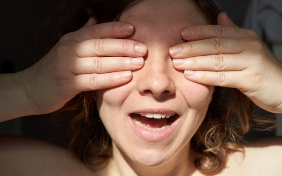Cheerful young caucasian woman covering eyes with hands in bright sunlight. photo