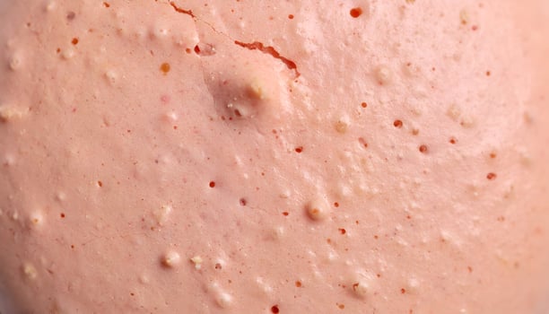 close-up macro texture of pink macaron shell surface with bumps and air holes, pastel bakery background, smooth and cracked baked crust photo