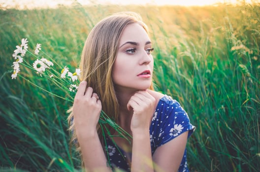 Girl sit in tall grass. A bouquet daisies in hand. photo