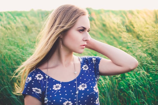 Girl blonde in a blue short tight dress sit in tall grass photo