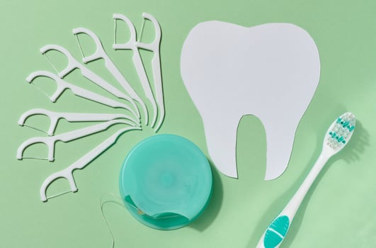 Flat lay composition of various dental hygiene products, including a green toothbrush, dental floss dispenser, a white dental floss pick, green background photo