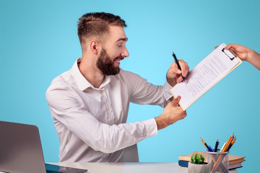 Millennial businessman in formal wear signing contract or agreement at desk in office, blue studio background. Young employee doing paperwork, sealing deal with new business partner photo