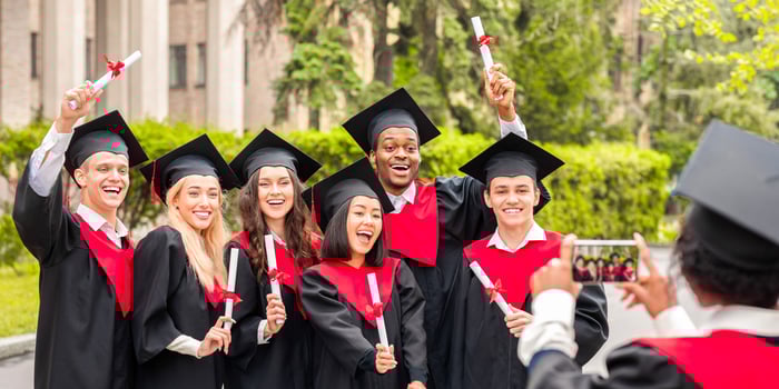 Emotional multiracial students having graduation party at university or college campus, taking photos on mobile phone. Happy international group of graduates posing together with diplomas