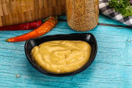 A bowl of mustard and a bottle of chili sauce on a wooden table photo
