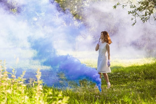 a woman in a white dress is standing in a field with blue smoke photo