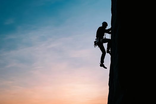A man climbing up a rock wall at sunset photo