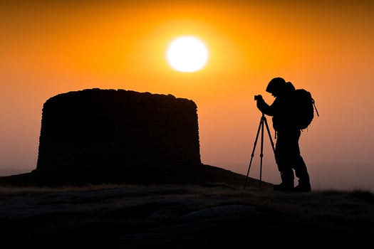 A man with a backpack and a tripod is taking a picture of the sunset photo