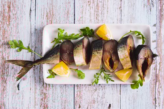 Close up of smoked mackerel pieces, lemon and arugula on a plate on the table top view photo