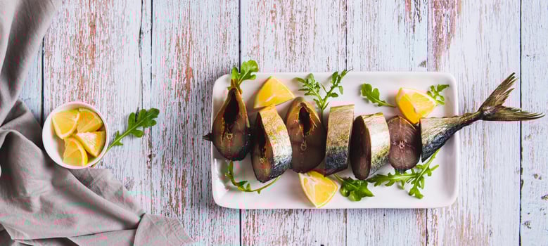 Smoked mackerel, lemon slices and herbs on a plate on the table top view web banner photo
