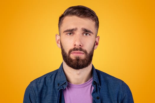 Millennial hipster guy feeling sad, lonely or depressed on grey studio background. Melancholic bearded man with unhappy face expression having trouble, suffering from stress or personal crisis photo