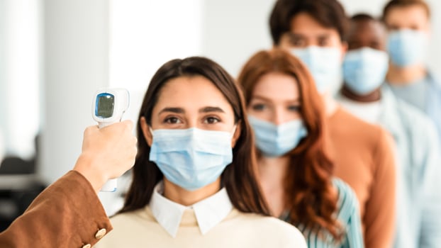 Woman Doing Temperature Screening Measuring Fever For Diverse People Standing In Queue, Using Infrared Contactless Themometer Indoors. Coronavirus, Covid-19 Pandemic Outbreak Concept photo