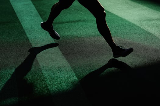Athlete running on green turf casts a long shadow during training photo