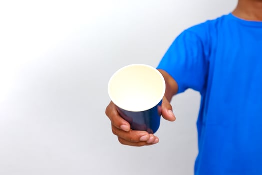 Person in blue shirt holding out a disposable paper cup against white background photo