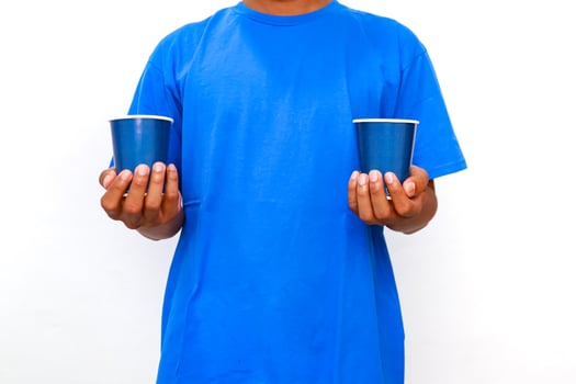 Person in blue shirt holding two blue paper cups against a white background indoors photo