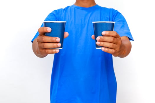 Person offering two blue paper cups against a clean white background studio shot photo