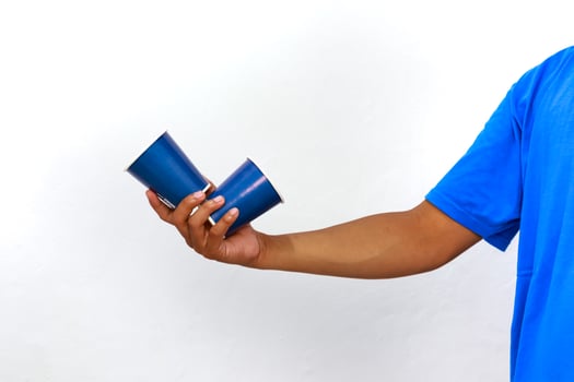 A man in a blue shirt holding two blue plastic cups on a white background photo