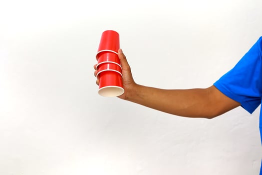 A person in a blue shirt holding a stack of red disposable cups on white background photo