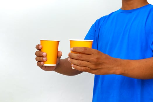 Man in blue shirt holding two yellow paper cups, isolated on white background, studio shot photo