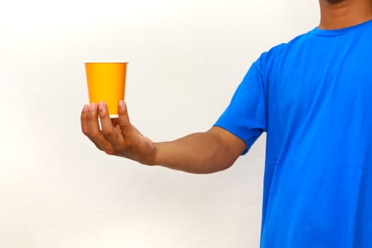 Person in Blue Shirt Holding Orange Cup Against White Background Presenting a Beverage photo