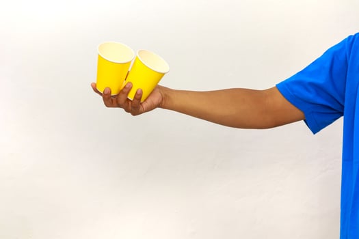 Arm holding two yellow paper cups against a white background in studio shot photo