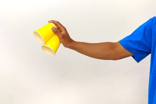 Hand holding two yellow paper cups in a blue shirt with a white background photo