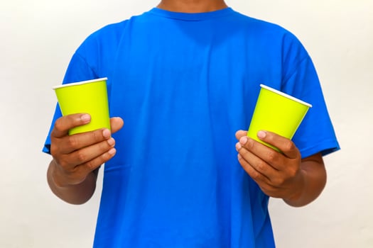 Person in blue shirt holding two light green disposable cups for serving drinks photo