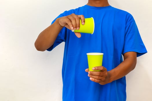 Person in Blue Shirt Pouring from a Yellow Cup into Another Against White Backdrop photo