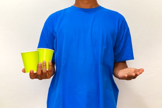 A person in a blue shirt holding two green paper cups and offering an empty hand photo