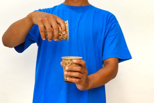 Person in blue t-shirt pouring liquid from one disposable cup into another, showcasing a simple action photo
