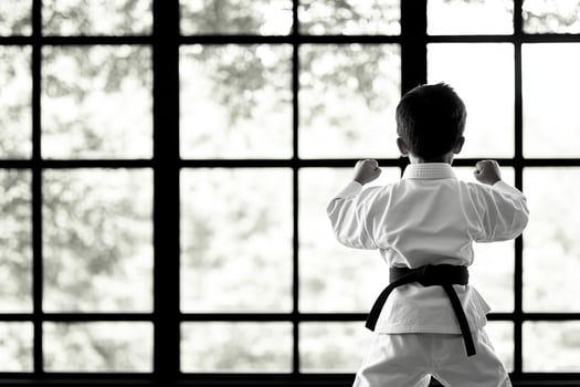 A young boy in karate gear standing in front of a window photo