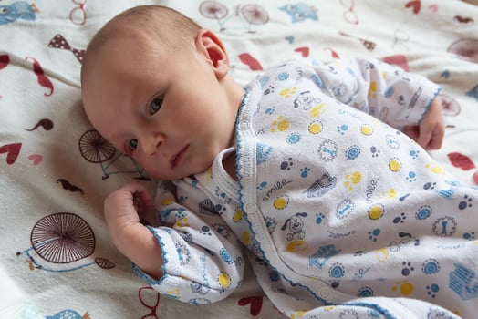 A newborn baby lies on the bed. People photo