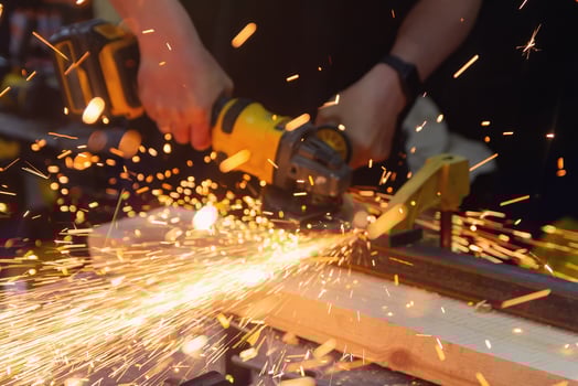 Craftsman using a grinder to cut metal in a workshop with sparks flying. Industry photo