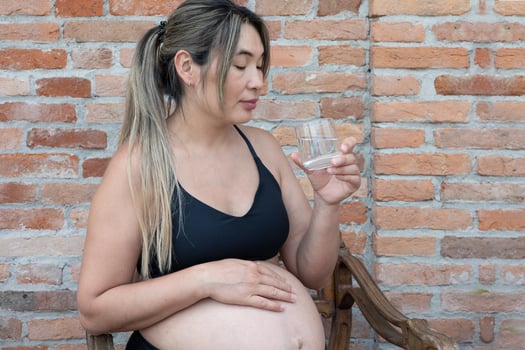 Pregnant woman wearing black top sitting and drinking a glass of fresh water while touching her belly with care, healthy lifestyle during pregnancy photo