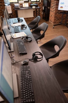Vacant collaboration space in modern office, featuring multiple desks, digital monitors and headsets, ideal for customer support team. Empty table neatly organized with devices for group of employees. photo