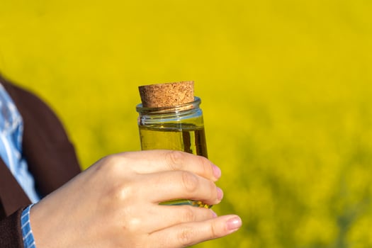 Hand Holding Small Glass Bottle with Cork Filled with Yellow Liquid Against a Floral Background photo