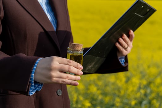 Examining Golden Liquid in Glass Container, Woman Holding Clipboard in Yellow Canola Field photo