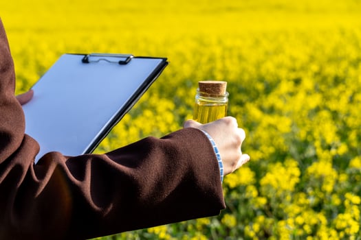 Agronomist Inspecting Canola Oil Quality in Field Holding Clipboard and Vial with Cork Stopper photo