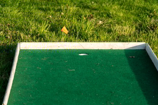 Close-up of a Miniature Golf Course Hole with Green Turf and Grass, Featuring a Small Orange Flag for Direction photo