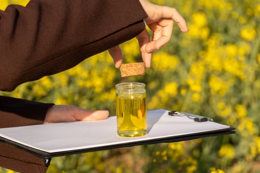 A researcher is examining the quality of biofuel by adding a sample to a glass jar while in a field of yellow flowers photo