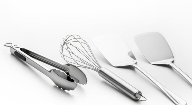 Gleaming stainless steel kitchen utensils tongs, whisk, and spatulas on white photo