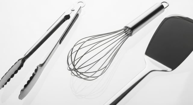 Stainless steel kitchen utensils tongs, whisk, and spatula on a white surface. photo