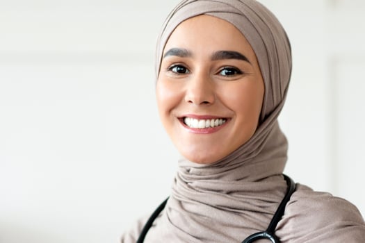 Cheerful doctor young woman in hijab posing at her workdesk in clinic, sitting in front of laptop and smiling at camera, copy space. Modern healthcare industry, muslim women employment concept photo