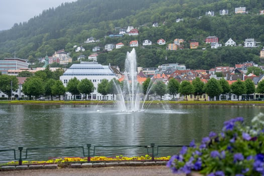 Bergen, Norway - July 7, 2024. Fountain in city park lake with colorful houses on hillside photo