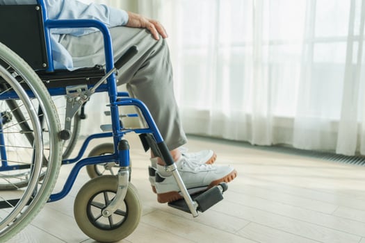 Senior man sitting in wheelchair near window in retirement hospital, legs feet close up. Old paralyzed man in chair for people with disability at home. Lonely elderly sick man sitting on wheelchair photo