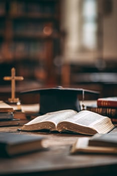 Books and Graduation Cap Placed on Wooden Table in Library During Daytime With Sunlight Filtering In photo