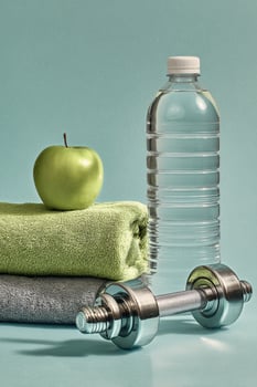 Fitness Essentials on a Pastel Background Featuring a Green Apple, Towel, Water Bottle, and Dumbbell photo